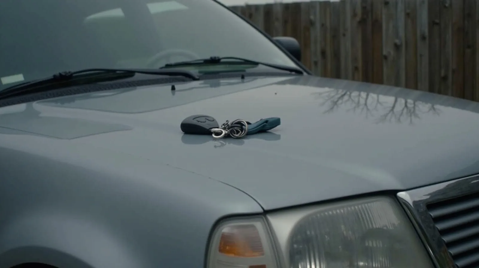A parked car with an insurance policy packet and keys resting on the hood